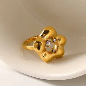 Detailopname van gouden matte bloemring met drie zirkoonstenen op keramisch dienblad