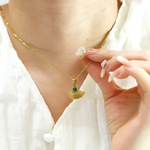 Gros plan d'un collier vintage doré avec éventail en malachite verte sur chemise blanche