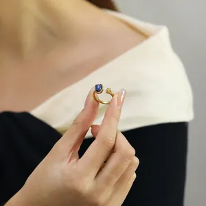 Detail of gold open ring featuring a blue cat-eye stone and delicate flower accent