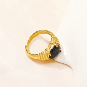 Dettaglio macro di anello vintage dorato con gemma nera ovale e fascia a righe tessuta