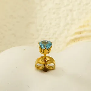 Macro d'une boucle d'oreille couronne dorée avec zircon bleu clair et serti à quatre griffes