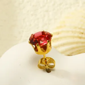Détail macro d'une boucle d'oreille couronne dorée avec une pierre de zircon rouge vif