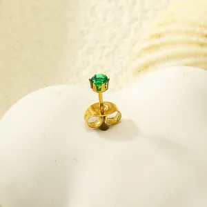 Gros plan d'un clou d'oreille en acier doré avec zircon vert sur support cœur blanc