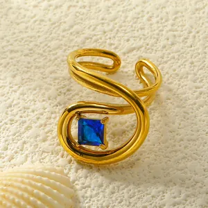 Detailansicht vergoldeter Spiralring mit blauem Zirkon auf sandigem Hintergrund