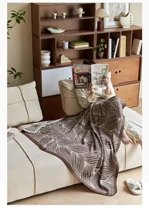 Detail of Nordic knitted throw blanket with brown leaf jacquard on a beige sofa