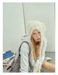 Close-up of white knit beanie with colorful dots and tassel earflaps on a model