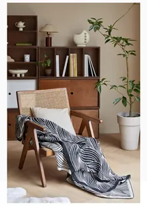 Close-up of black and white wavy leaf pattern knit throw blanket on a wooden rattan chair
