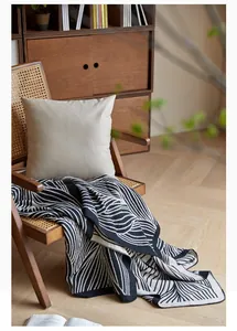 Detail of Nordic jacquard leaf knit blanket and beige pillow on a wicker chair