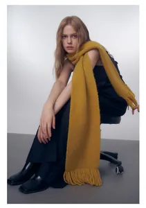 Dettaglio di una sciarpa lavorata a mano giallo acceso con frange su una modella di moda