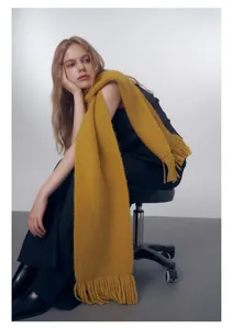 Dettaglio di morbida sciarpa in maglia giallo zenzero con lunghe frange e trama spessa e soffice