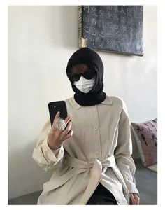 Detalle de un pasamontañas de punto negro con una gabardina beige para el invierno
