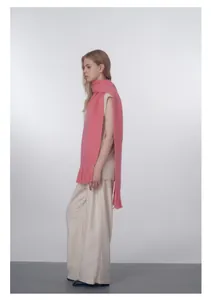 Sciarpa di maglia rosa con lunghe frange abbinata a gilet senza maniche e pantaloni beige