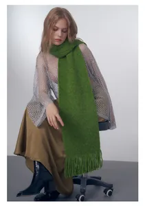 Dettaglio di sciarpa in maglia verde erba con lunghe nappe decorative sulle estremità