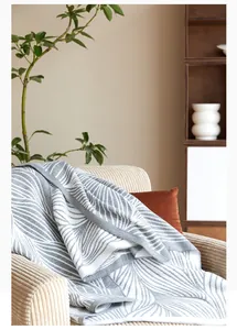 Detail of Nordic knit blanket with leaf pattern texture on a light corduroy sofa