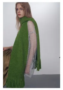Dettaglio di una sciarpa in maglia spessa verde erba con lunghe frange e consistenza