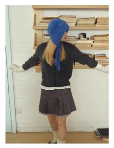 Detail of blue plush tie-on beanie with grey knitted cardigan and pleated skirt ensemble