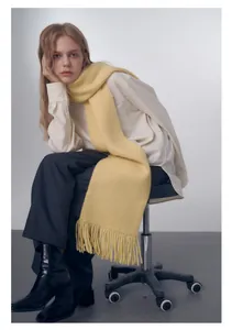 Dettaglio di una morbida sciarpa in maglia giallo tenue con texture e frange