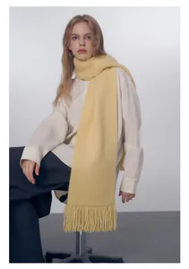 Dettaglio della sciarpa in maglia giallo chiaro con trama a coste e frange a nappa