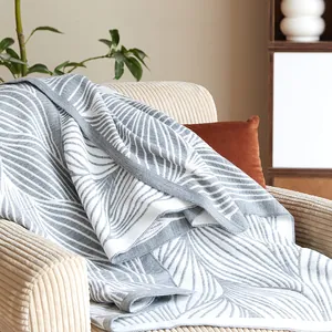 Nordic leaf pattern knit blanket in grey and white draped over a beige corduroy sofa