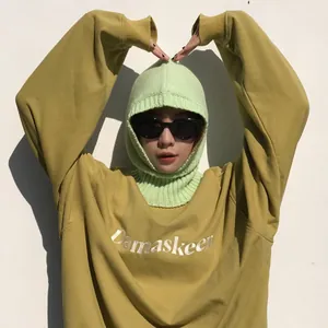 Mujer con sudadera mostaza y pasamontañas de lana de punto verde claro al aire libre