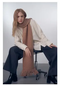 Dettaglio di sciarpa in maglia marrone avena con frange abbinata a pantaloni larghi e stivali