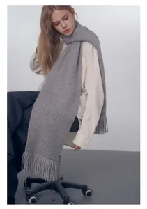 Dettaglio di una sciarpa grigia in maglia spessa con trama a coste e frange su una modella