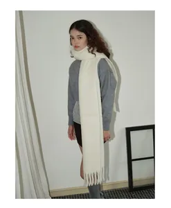 Detailansicht eines dicken weißen Wollschals mit Fransen über einem grauen Strickpullover