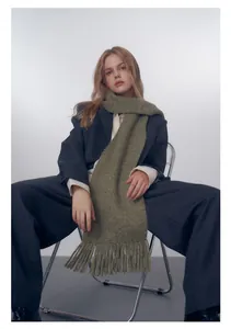 Dettaglio della sciarpa in maglia verde oliva con lunghe frange e trama di lana