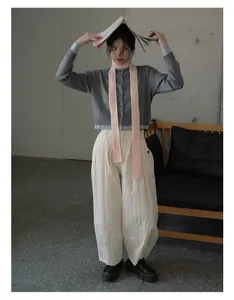 Full body look of a pink slim knit wool scarf paired with a grey cardigan and white pants