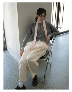 Detail of pink knitted narrow scarf styled with grey cardigan and white quilted trousers