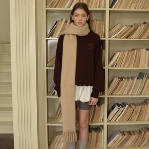 Beige wool blend oversized scarf with long tassels worn with a brown sweatshirt in a library