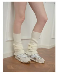 Close-up of cream knitted lace leg warmers styled with retro sneakers on wooden floor