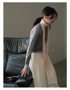 Close-up of a pink knitted narrow scarf styled with a grey blue cardigan and beige pants