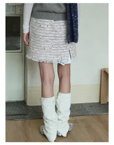 Dettaglio di scaldamuscoli in maglia bianca con gonna in tweed e scarpe argentate
