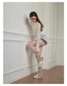 Close-up of beige knitted leg warmers with lace trim worn with stylish silver sneakers