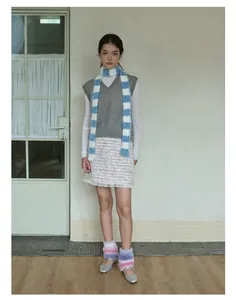 Detail view of a blue and white striped long scarf with grey knit vest and tweed skirt