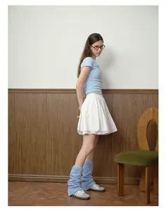 Dettaglio di scaldamuscoli in maglia azzurra abbinati a gonna a pieghe bianca e sneakers