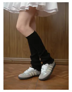 Close-up of black ribbed knit leg warmers styled with suede sneakers and white skirt