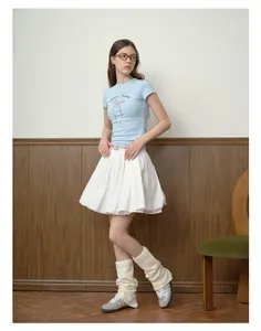 Dettaglio di scaldamuscoli in maglia crema abbinati a gonna a pieghe bianca e sneakers