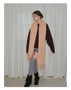 Detail eines pfirsichfarbenen Strickschals mit dicken Fransen an einem modernen Model