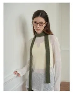 Dettaglio di una sciarpa in maglia stretta verde scuro abbinata a un maglione bianco chic