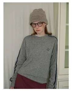 Detail of grey crewneck sweatshirt featuring navy sleeve stripes and woven chest logo patch