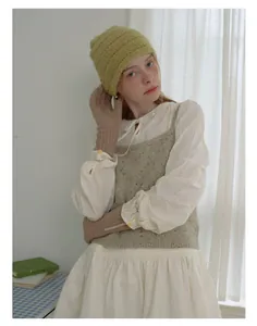 Detailed layering of yellow knit beanie with grey vest and khaki buttoned gloves