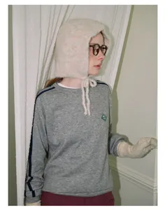 Detail of soft cream plush knit hat with tie straps paired with a gray sweatshirt