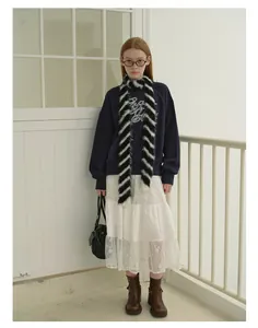 Dettaglio di una sciarpa in maglia a righe bianche e nere con felpa blu scuro coordinata