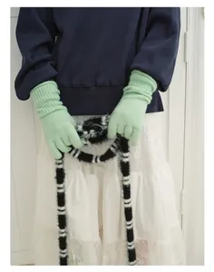 Close-up of mint green knitted gloves with a black and white striped faux fur scarf