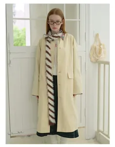 Dettaglio di una sciarpa in maglia a righe abbinata a un cappotto beige e maglieria bianca