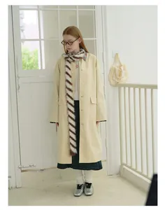 Dettaglio di una sciarpa in maglia a righe marroni e bianche su un trench beige