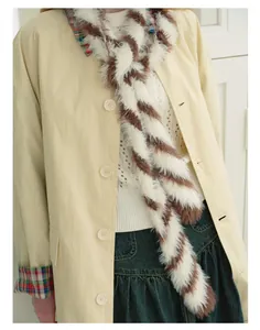 Dettaglio di una sciarpa a righe marroni e bianche abbinata a un trench coat beige