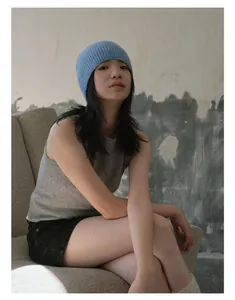 Bonnet en laine bleue à côtes porté avec un gilet gris par un mannequin assis